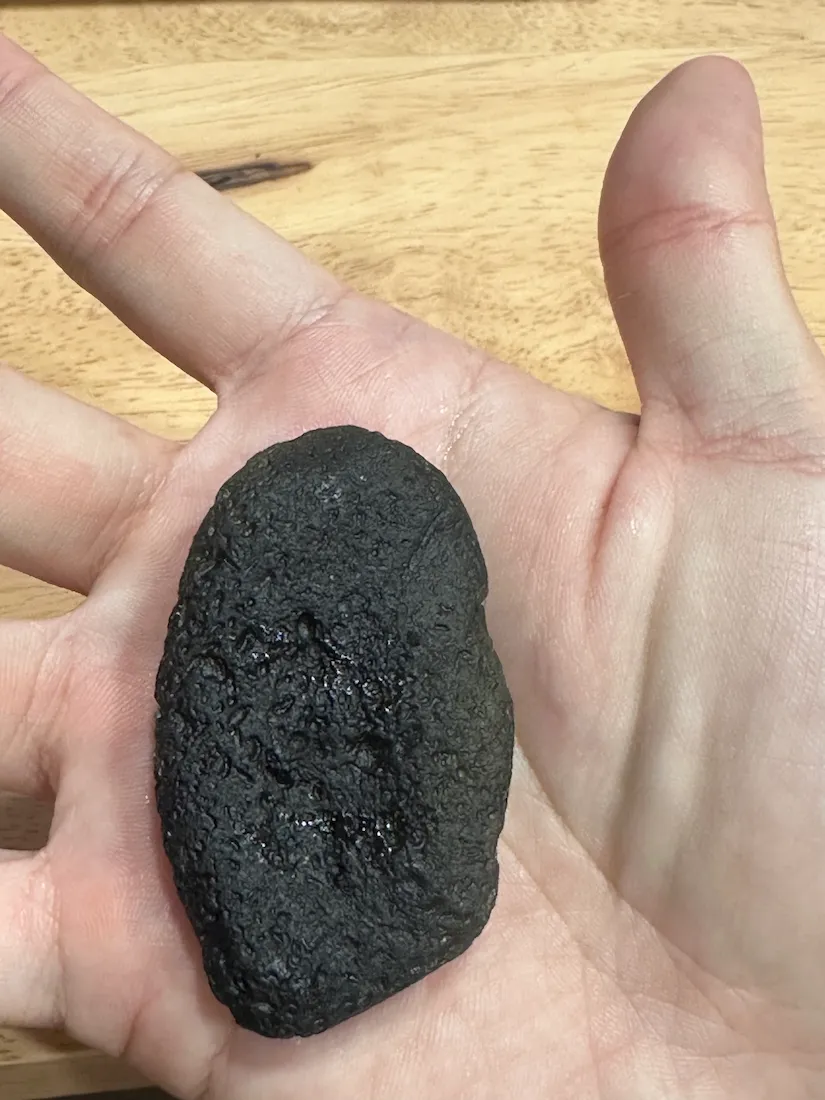 50克捷克隕石掌心實拍照。厚實沉穩原礦手感，滿布天然火山與隕石撞擊蝕變氣印紋。 | Bohemian Impactite with Natural Sculpting Moldavite. This giant specimen exhibits flawless aerodynamic pitting (sculpting). A true holy grail for collectors.